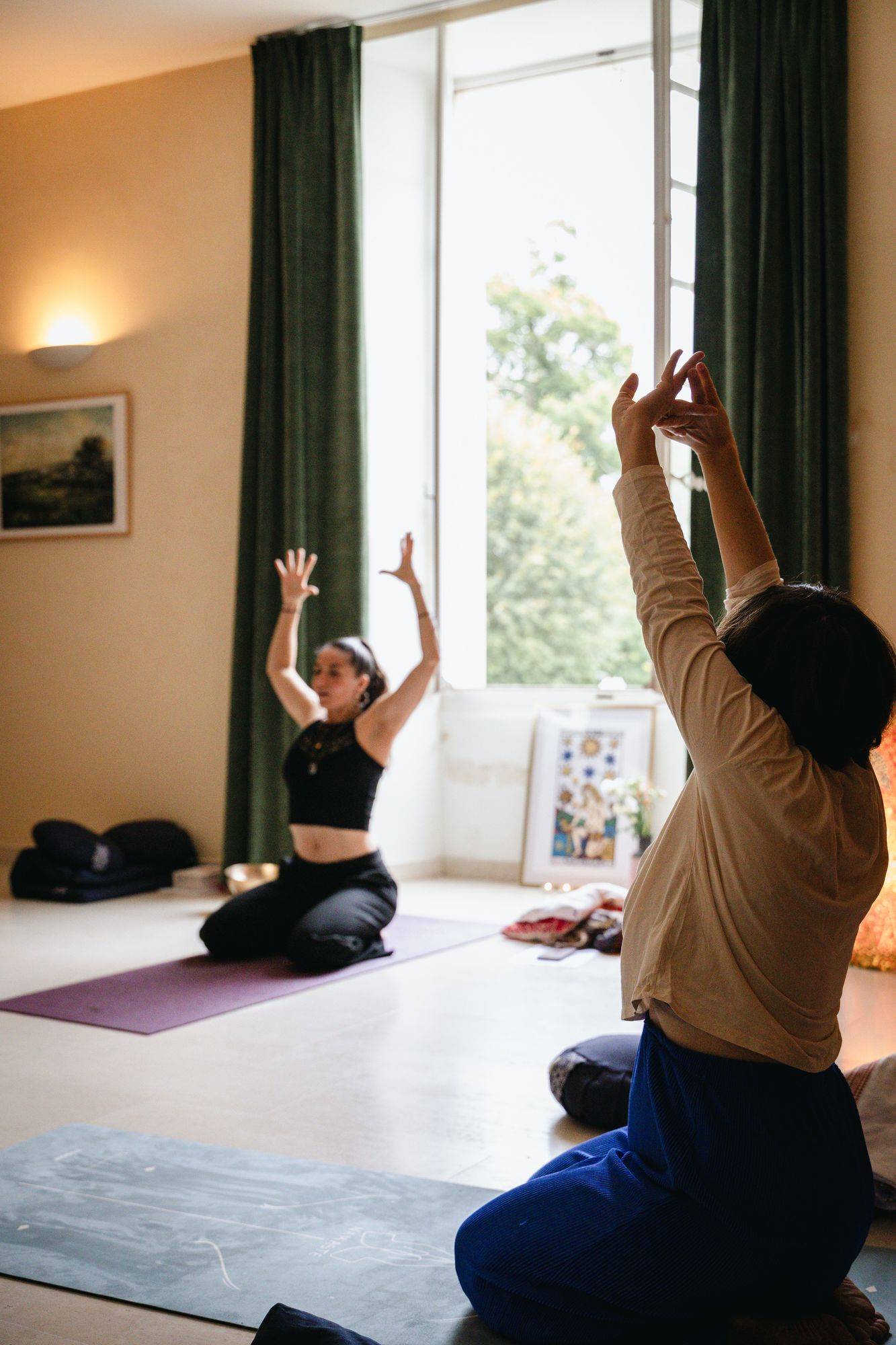 Susana guide une séance de yoga, bras levés, face à une participante
