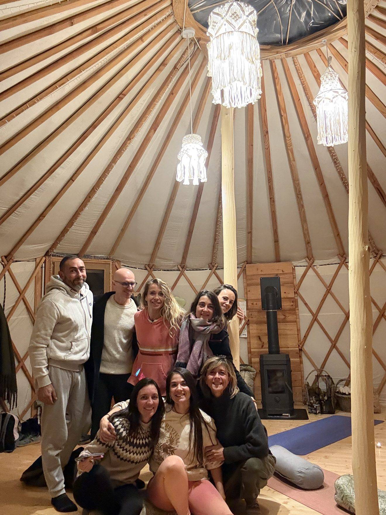 Les participantes et participants de L'Art du bilan réunis et souriants à l'intérieur de la yourte éclairée par des suspensions en macramé