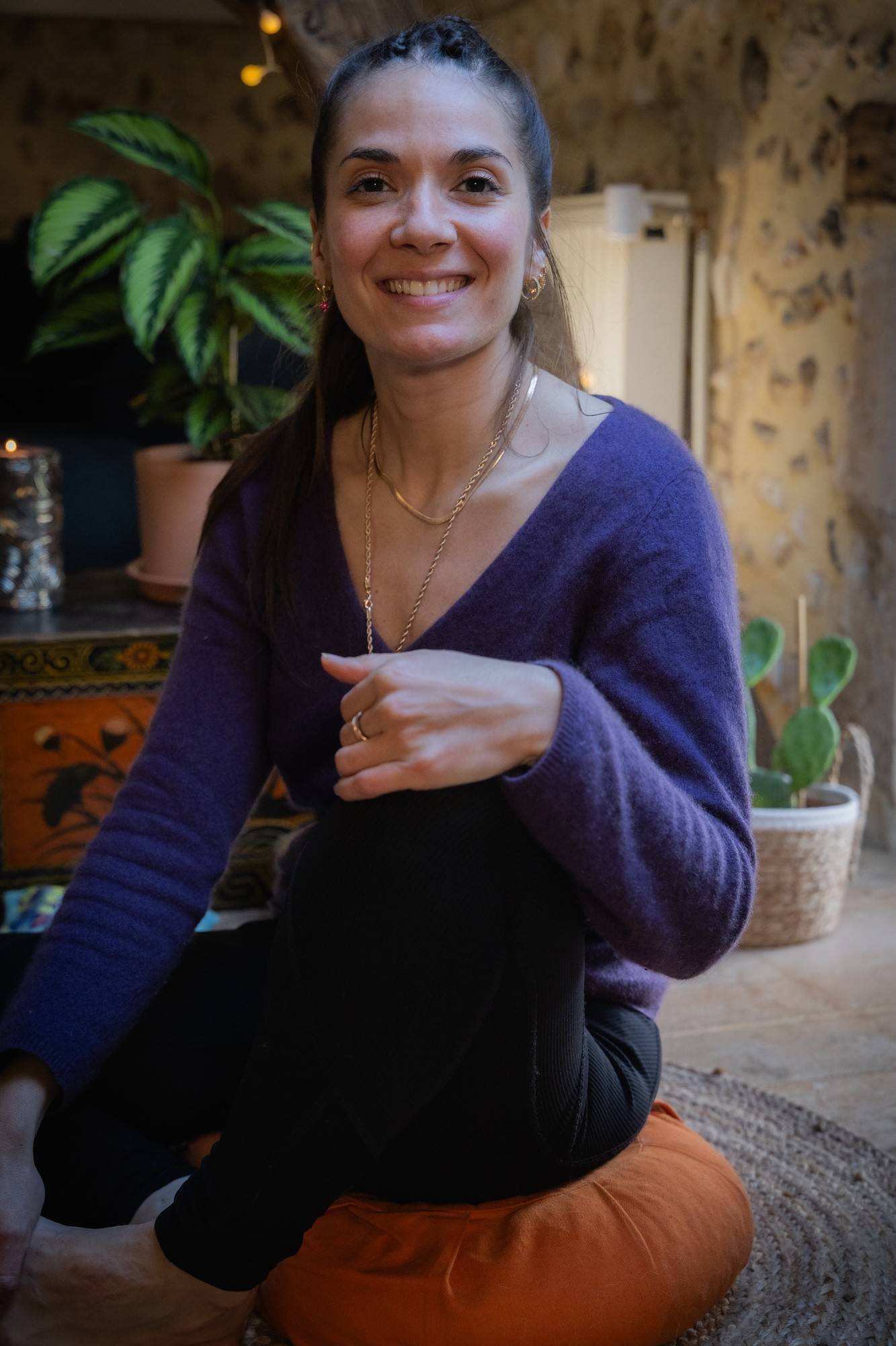 Susana d'Arcambel souriante, assise sur un coussin de méditation, dans un pull violet